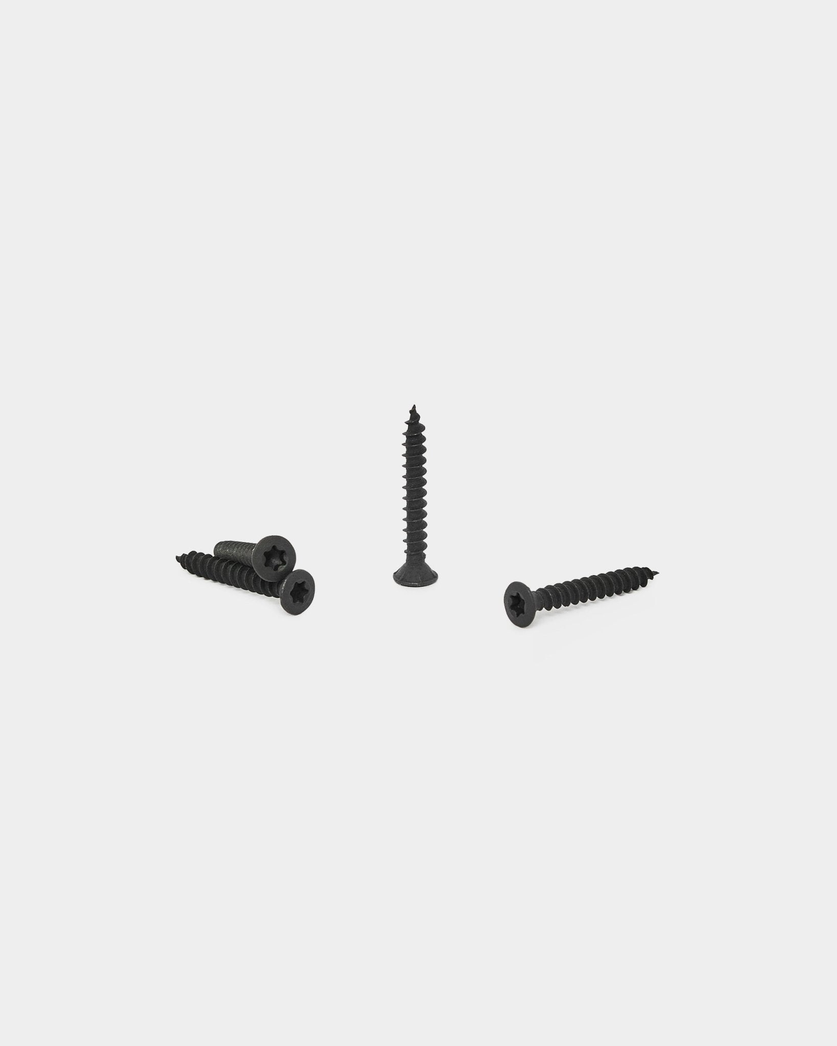 Four black WoodUpp Installation Screws, three lying flat and one upright, displayed on a white background for Akupanel acoustic panel installation.