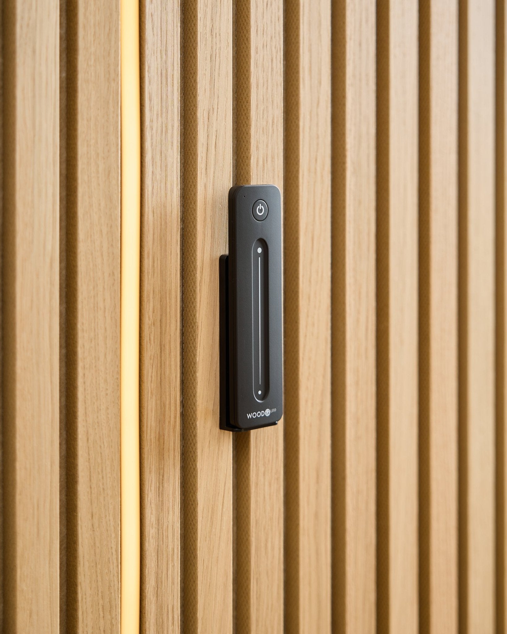A WoodUpp Lumi | Remote / LED Striplight is installed on a light wood acoustic panel, with a yellow cable visible behind the wooden slats.