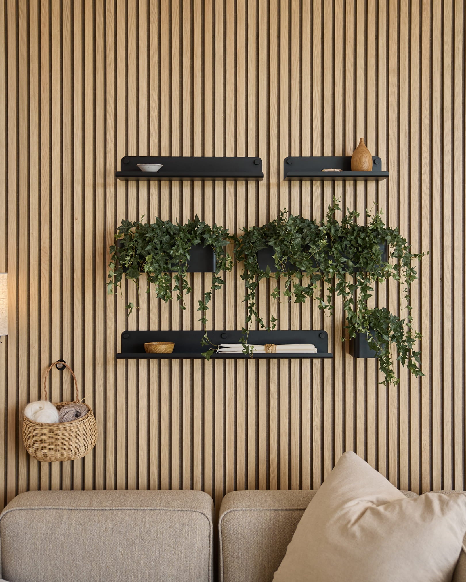Modern living room featuring a Nordic acoustic slatwall panel, black shelves, trailing plants in WoodUpp’s Norr Plant Box (35.9 cm, Black), and a beige sofa.