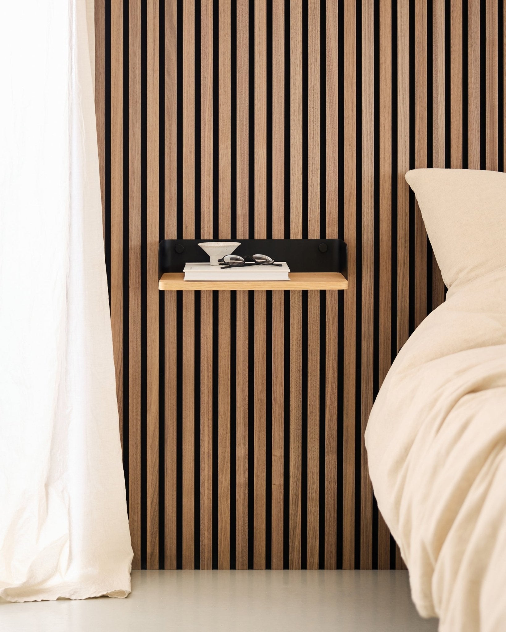 Minimalist bedroom with a Nordic wood slat acoustic panel wall, WoodUpp Linn Bookshelf in Natural Oak, and a floating nightstand beside a beige bed.