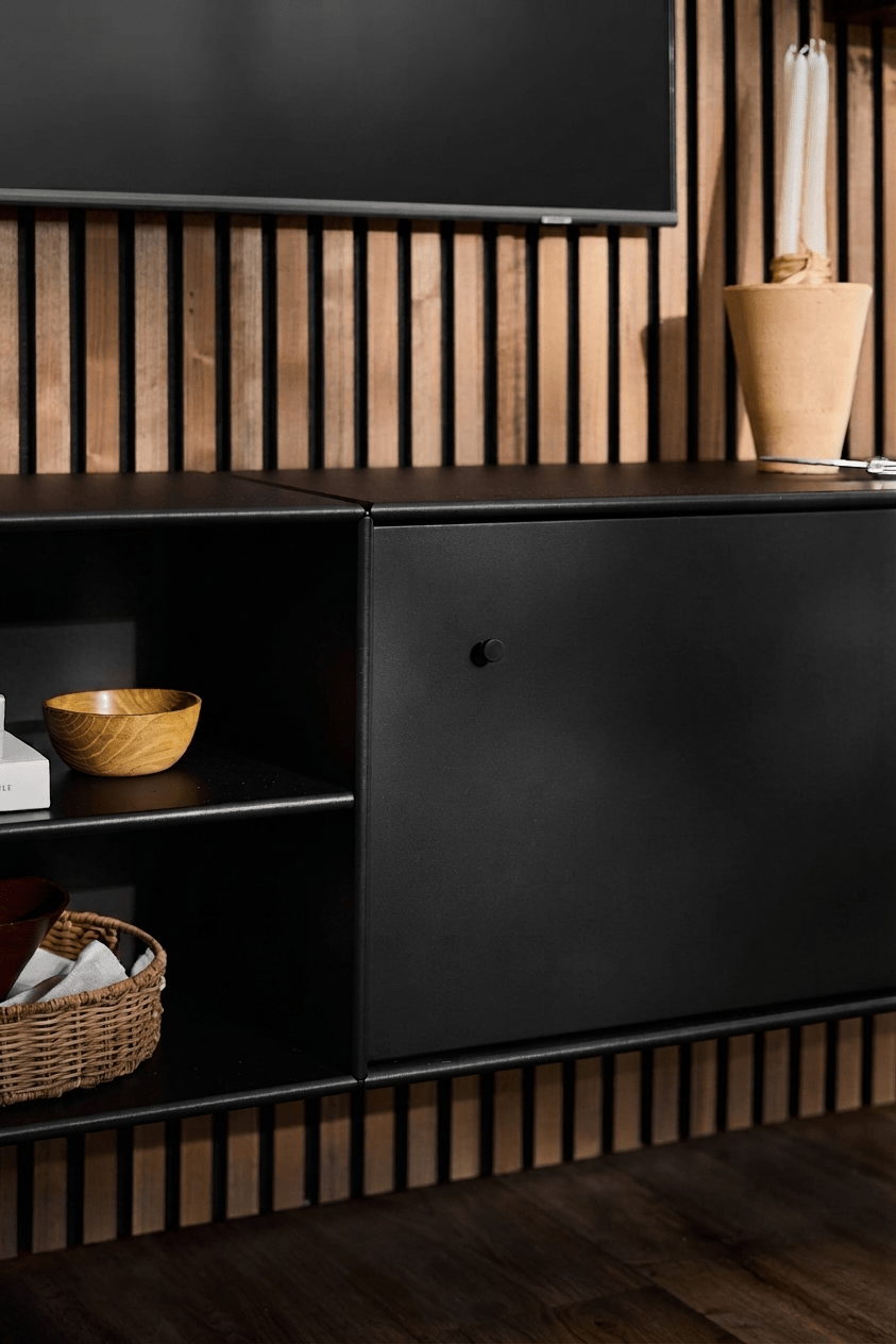 Black WoodUpp Arka TV Console with open shelves for books and baskets, tan vase, smart cable management, and vertical Akupanel acoustic wood panel backdrop.