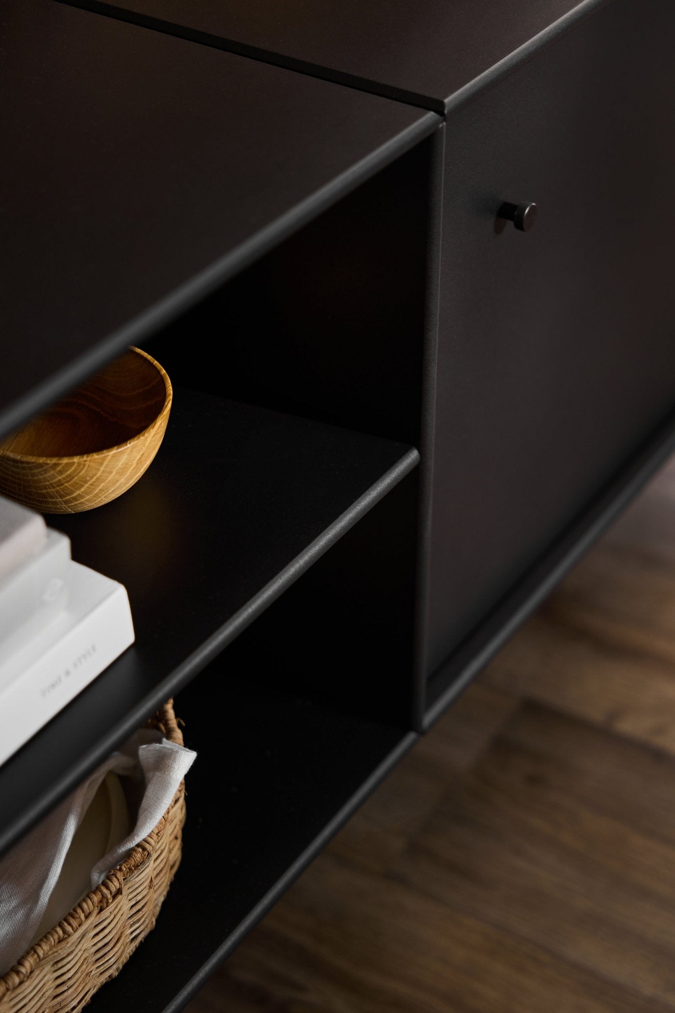 Schwarze Arka-TV-Konsole von WoodUpp im minimalistischen Design, konzipiert für die Kabelführung und Aufbewahrung, auf einem Holzboden platziert.