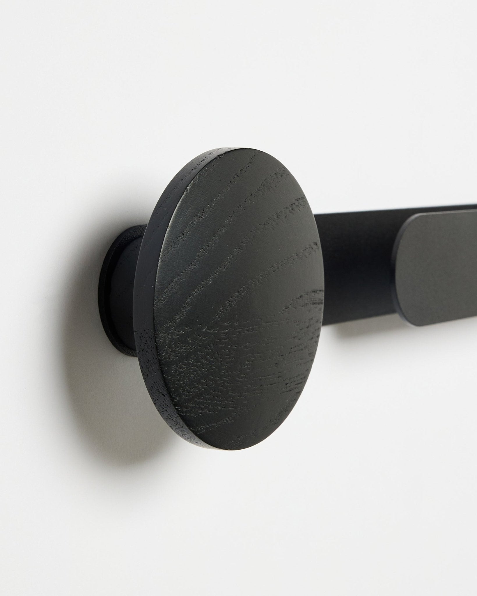 Close-up of the WoodUpp Linn | Horizontal Hanger in Black Oak, matte black finish, mounted on a white wall; accessory for acoustic wood panels.
