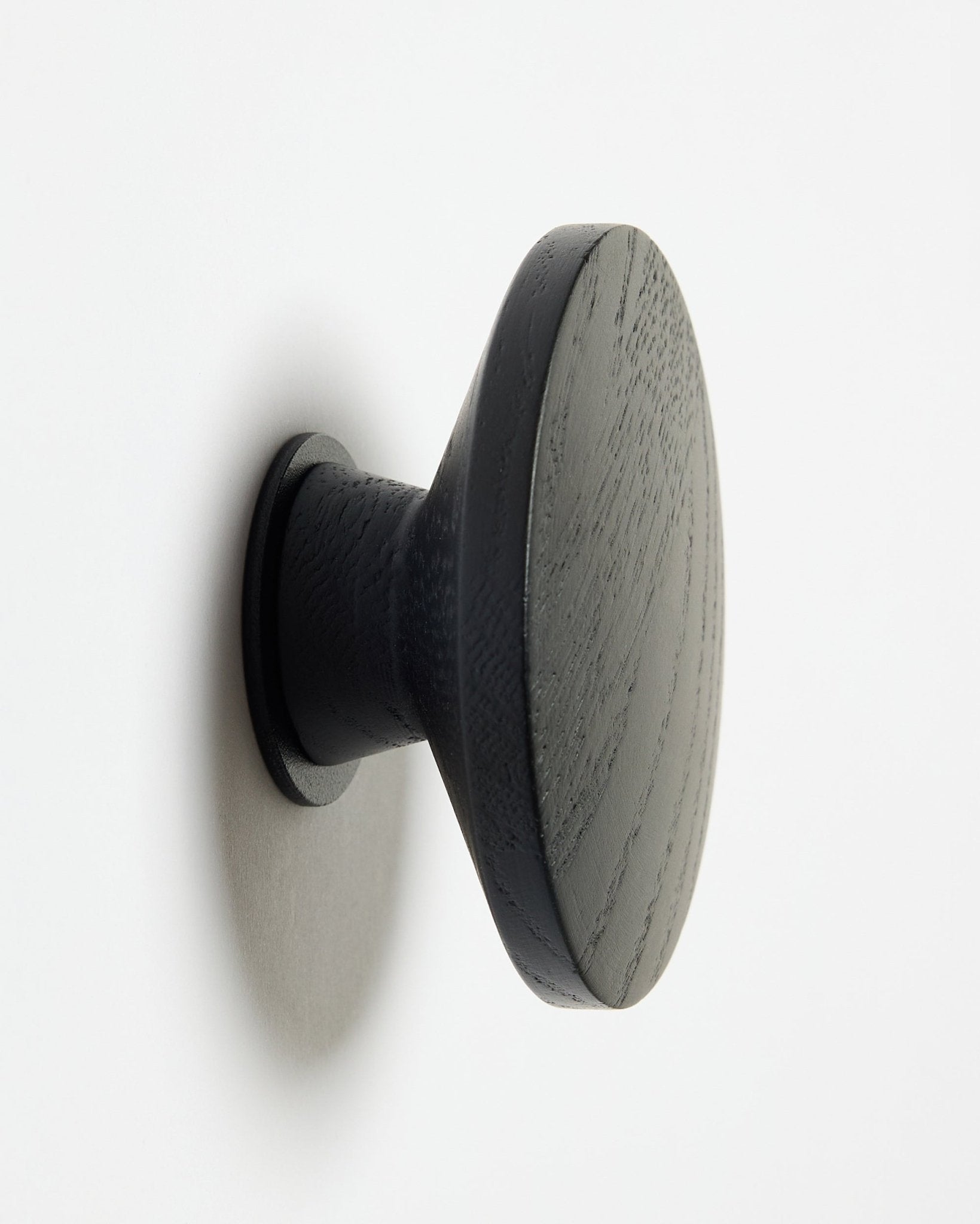 A round, black oak Linn | Single Hanger by WoodUpp, designed as an accessory for Akupanel acoustic wood panels, mounted on a white surface with a soft left shadow.