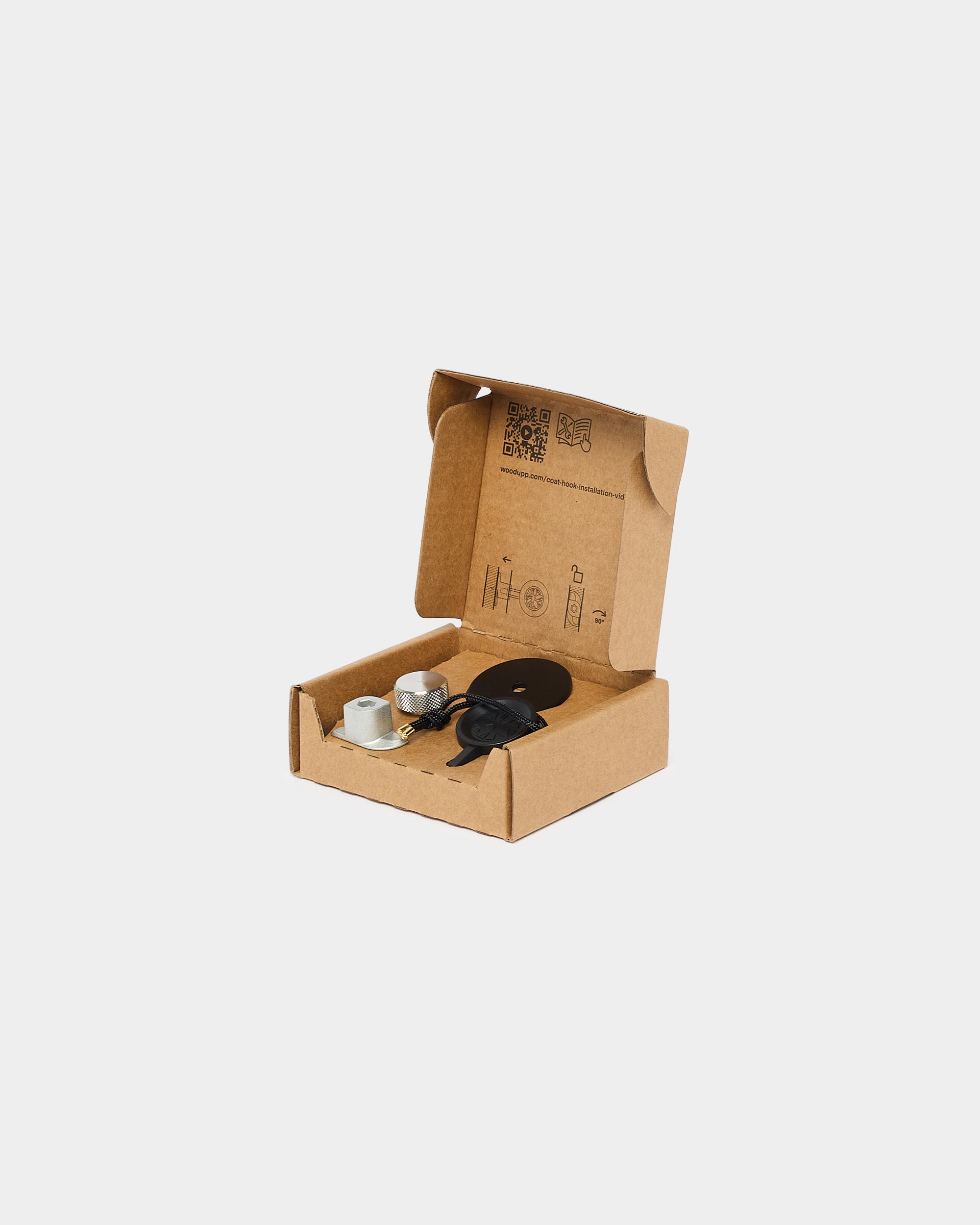 Open brown cardboard box containing two metal cylinders, a black cable, and a round black object, shown on a white background; components for acoustic panel installation.