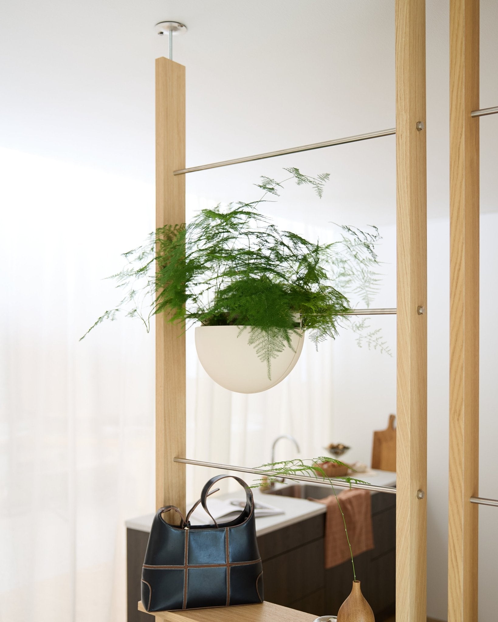 A Gro Soft Pocket (4L) by WoodUpp is mounted on a wooden frame above a black handbag in a bright, modern kitchen.