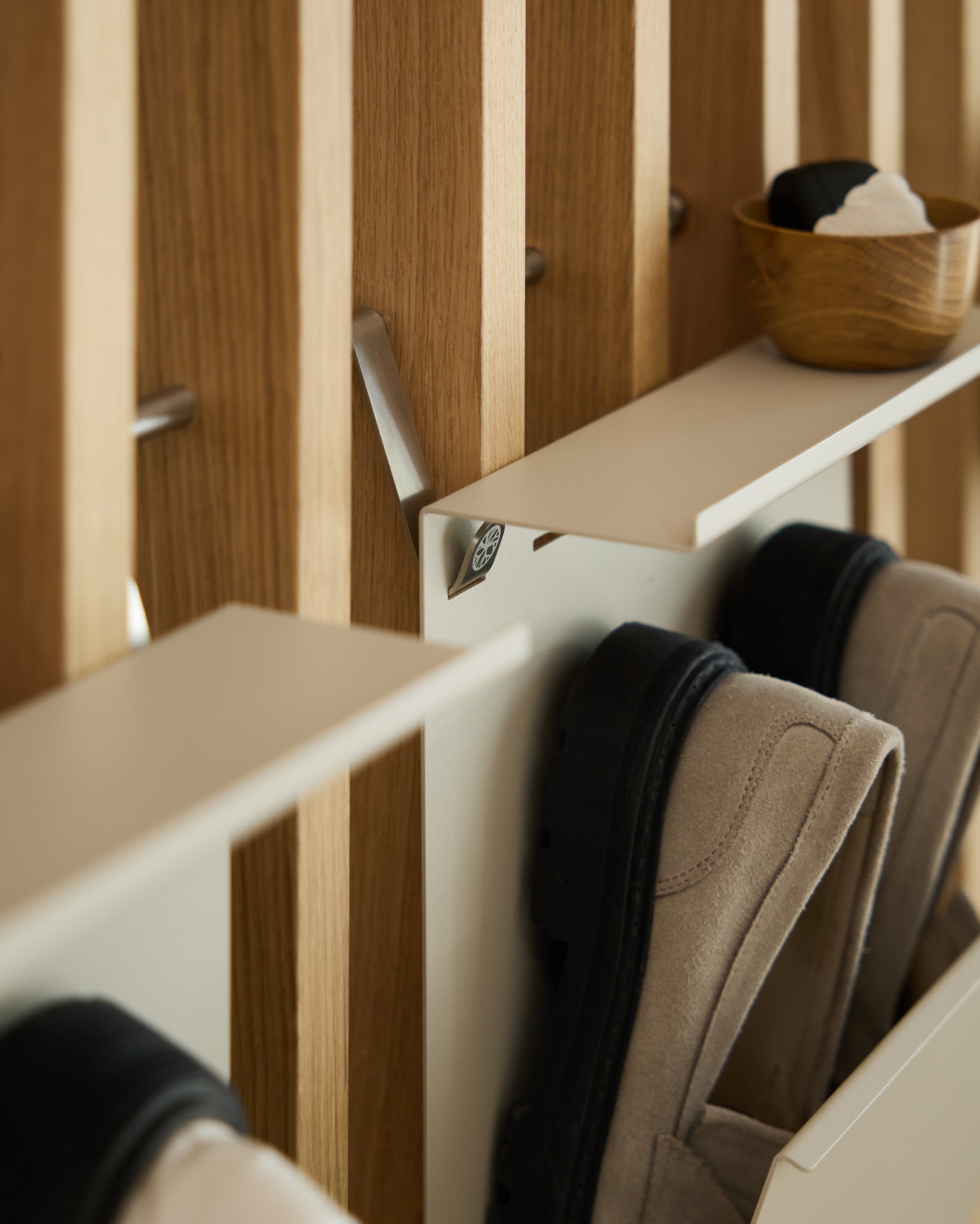 Minimalist beige powder-coated steel shoe rack by WoodUpp mounted on a Nordic slatted acoustic panel, with a small bowl for keys placed above.