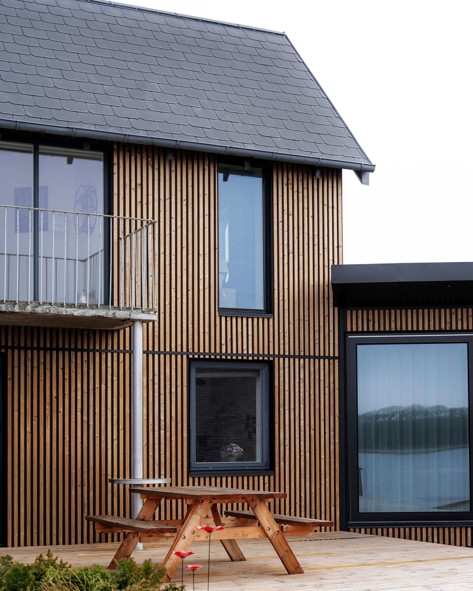 Modern house with WoodUpp Aluwood facade panels in Oiled Brown, featuring large windows, a balcony, and a deck with a wooden picnic table.