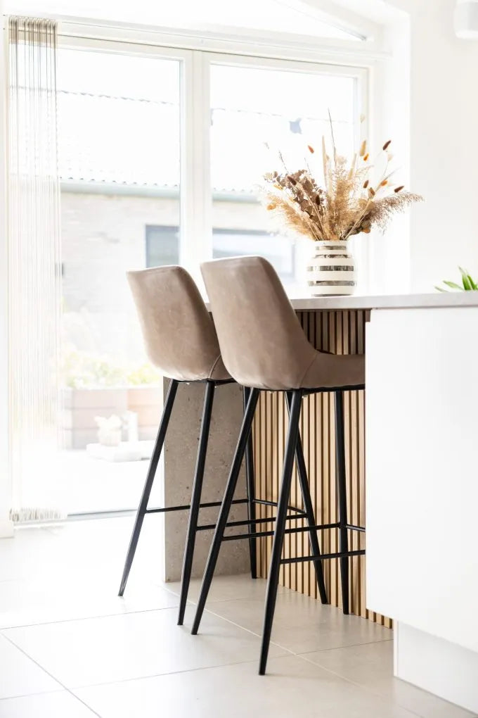 Beige bar stools at a kitchen island with a vase of dried flowers, large windows, and Nordic contemporary style featuring acoustic panels on the walls.