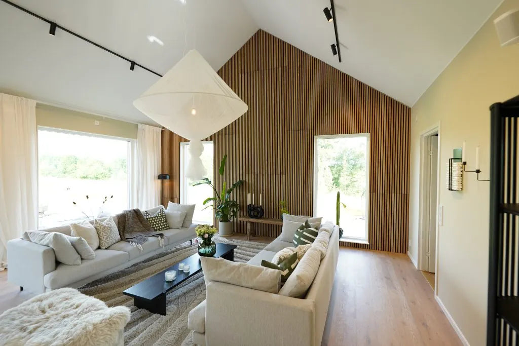 Modern living room with high ceiling, large windows, light sofas, Akupanel acoustic wood accent wall, indoor plants, and abundant natural light.