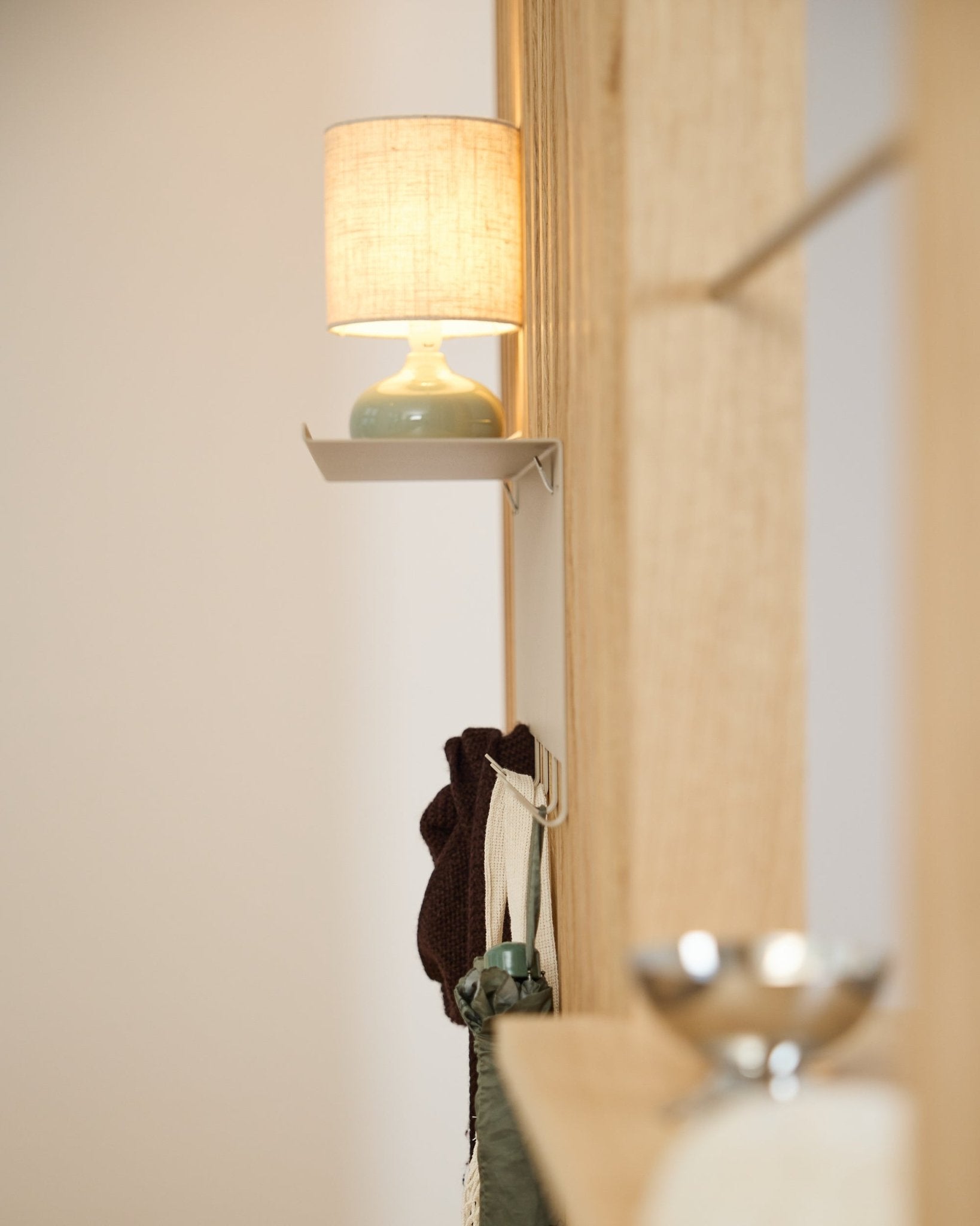 A beige WoodUpp Nell Coat Rack BM1 (63.5 x 24 cm) stands beneath a small table lamp next to a light Nordic wood acoustic panel wall.